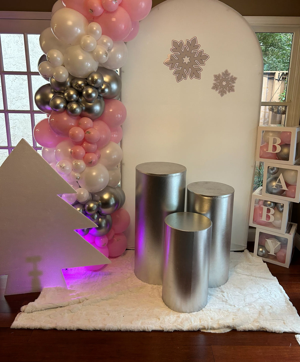 Pink white and silver balloon decoration with silver cylinder pedestals and purple accent lighting.
