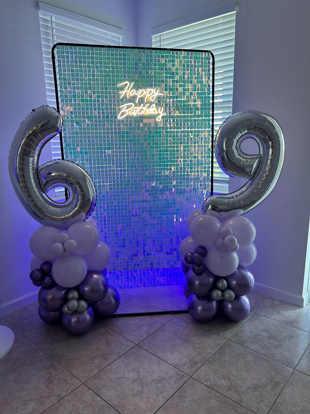 Iridescent sequin wall with illuminated Happy Birthday sign, purple accent lights and balloon number columns.