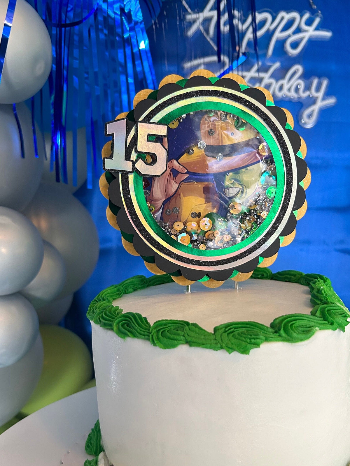Green and yellow movie-themed topper with age fifteen displayed on a white cake with green frosting.