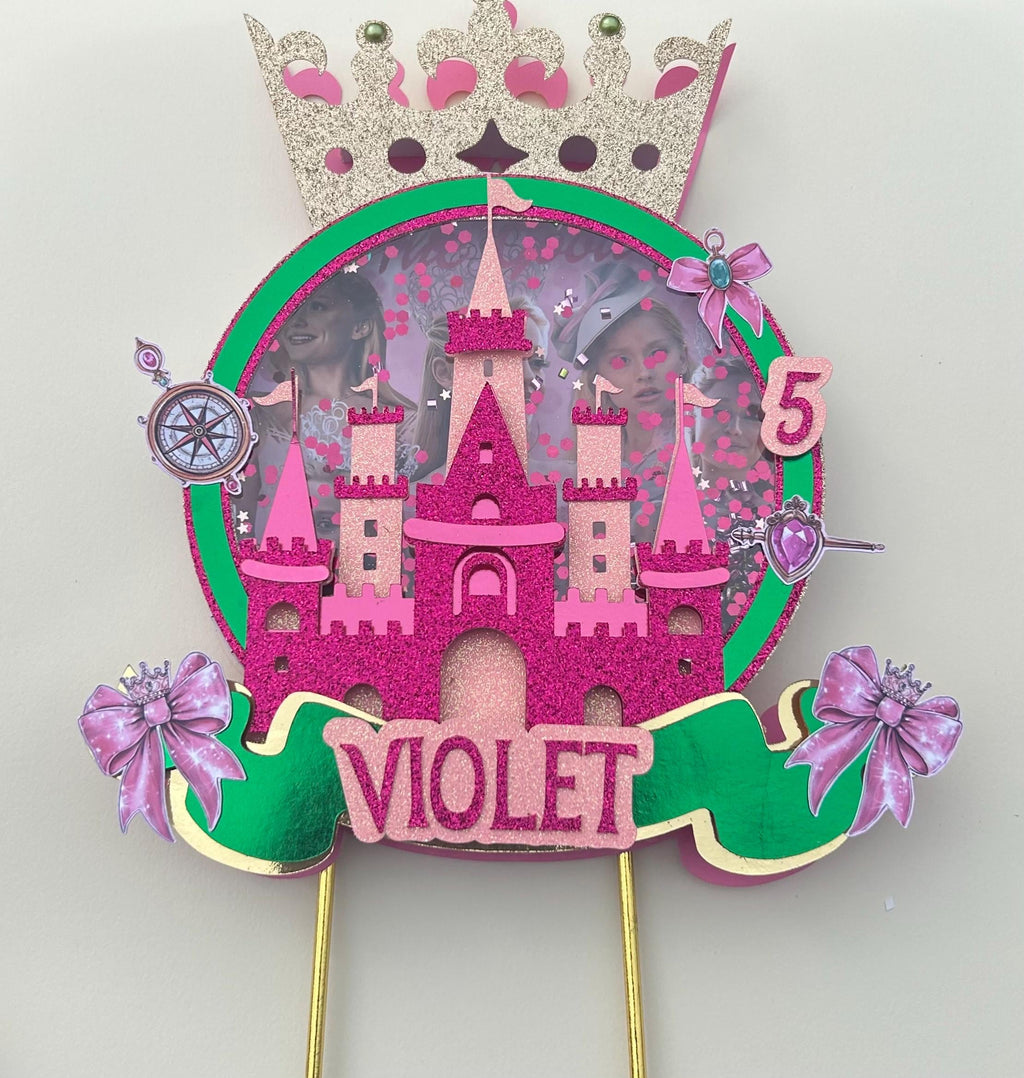 Pink castle birthday topper personalized with Violet and age five, gold crown, bows, green accents, and two gold sticks.