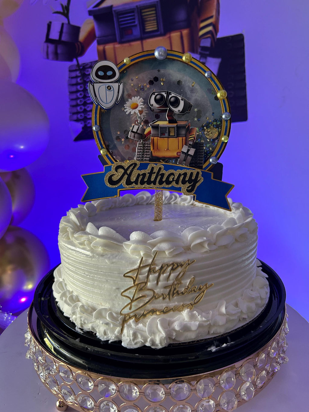 Personalized Anthony robot topper on a white frosted cake with a large robot party decoration in the background.