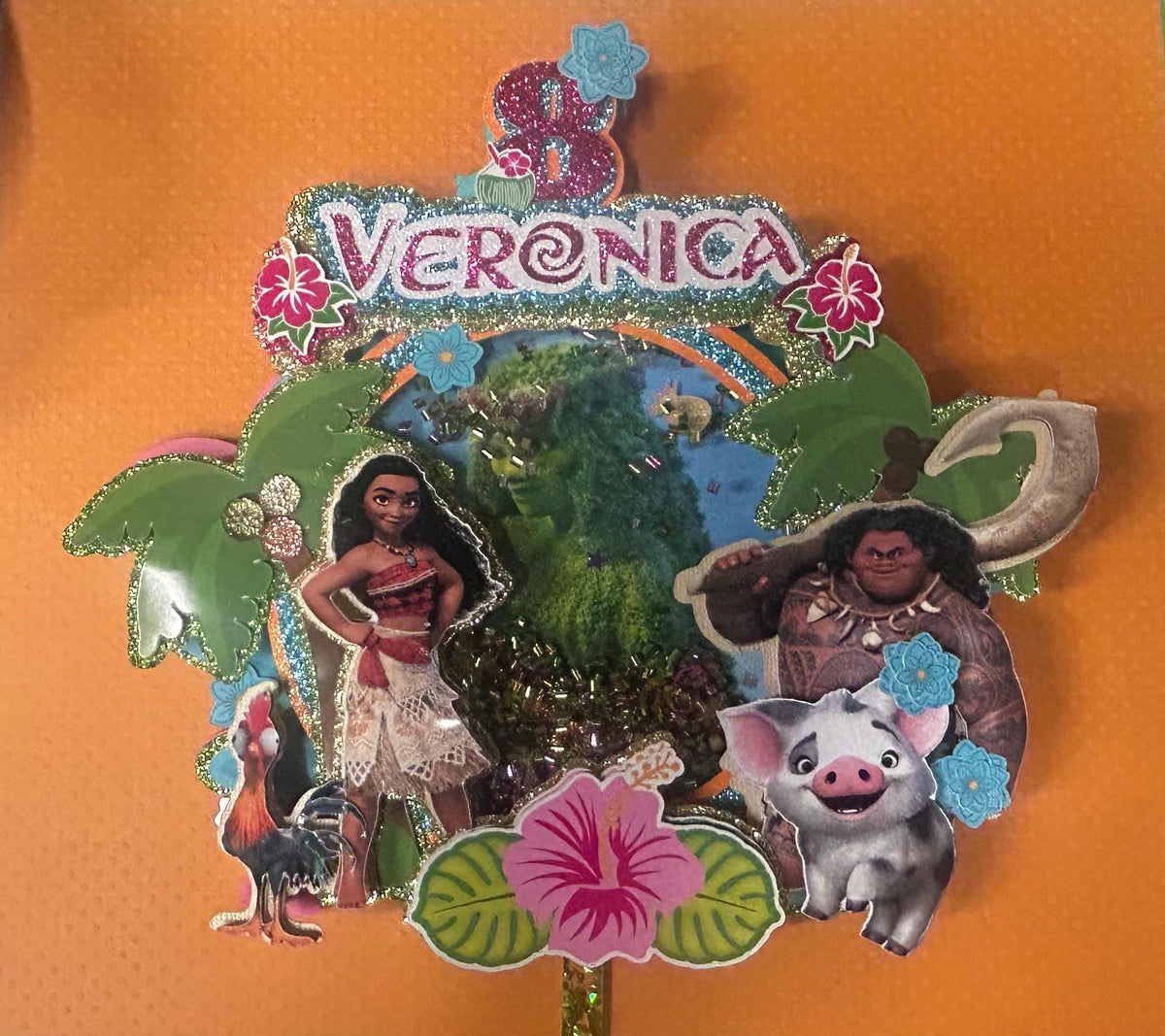 Close view of Veronica tropical cake topper with girl and demigod, pig, rooster, palm trees, flowers, and island background.