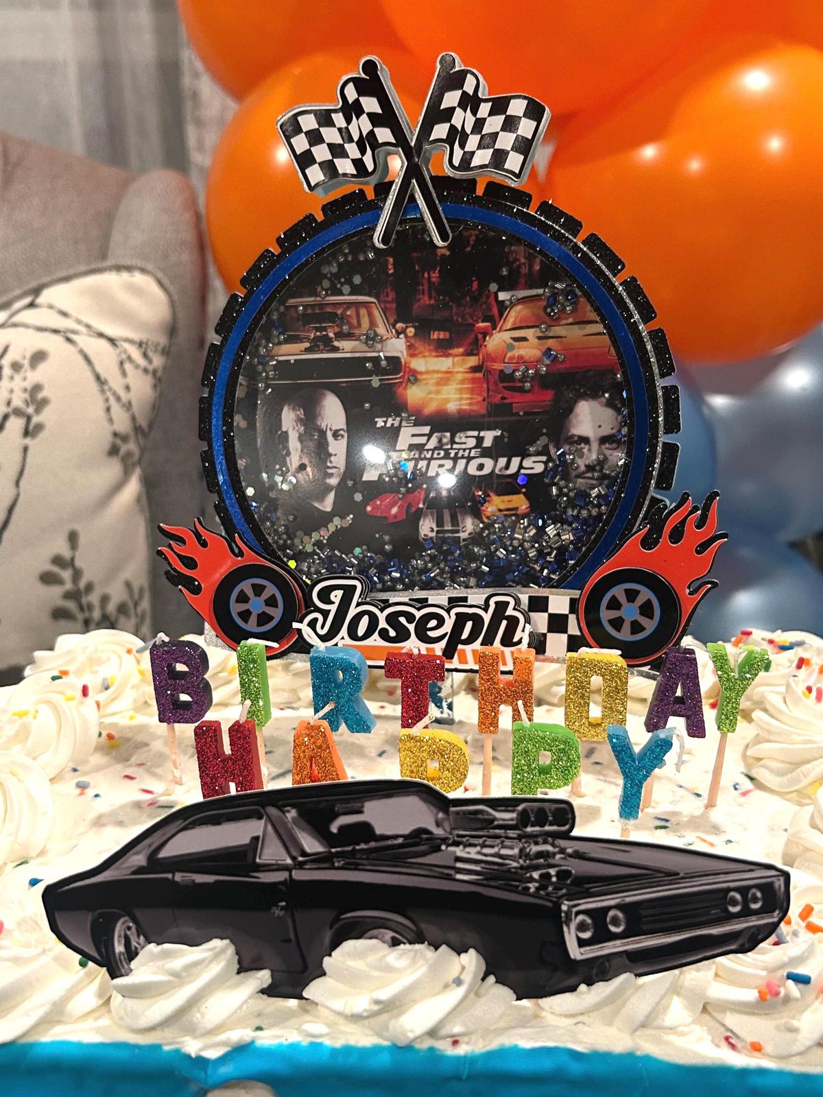 Personalized Joseph racing cake topper with checkered flags, red flames, black muscle car, and colorful birthday letter picks.