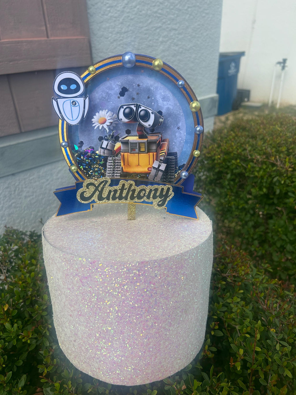 Personalized Anthony robot cake topper with a yellow tracked robot, white floating robot, circular sequin center, and blue banner.