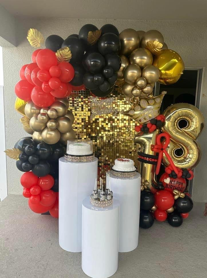 Red, black and gold balloon decoration with a gold sequin wall, white cylinder pedestals and a separate age balloon bouquet.